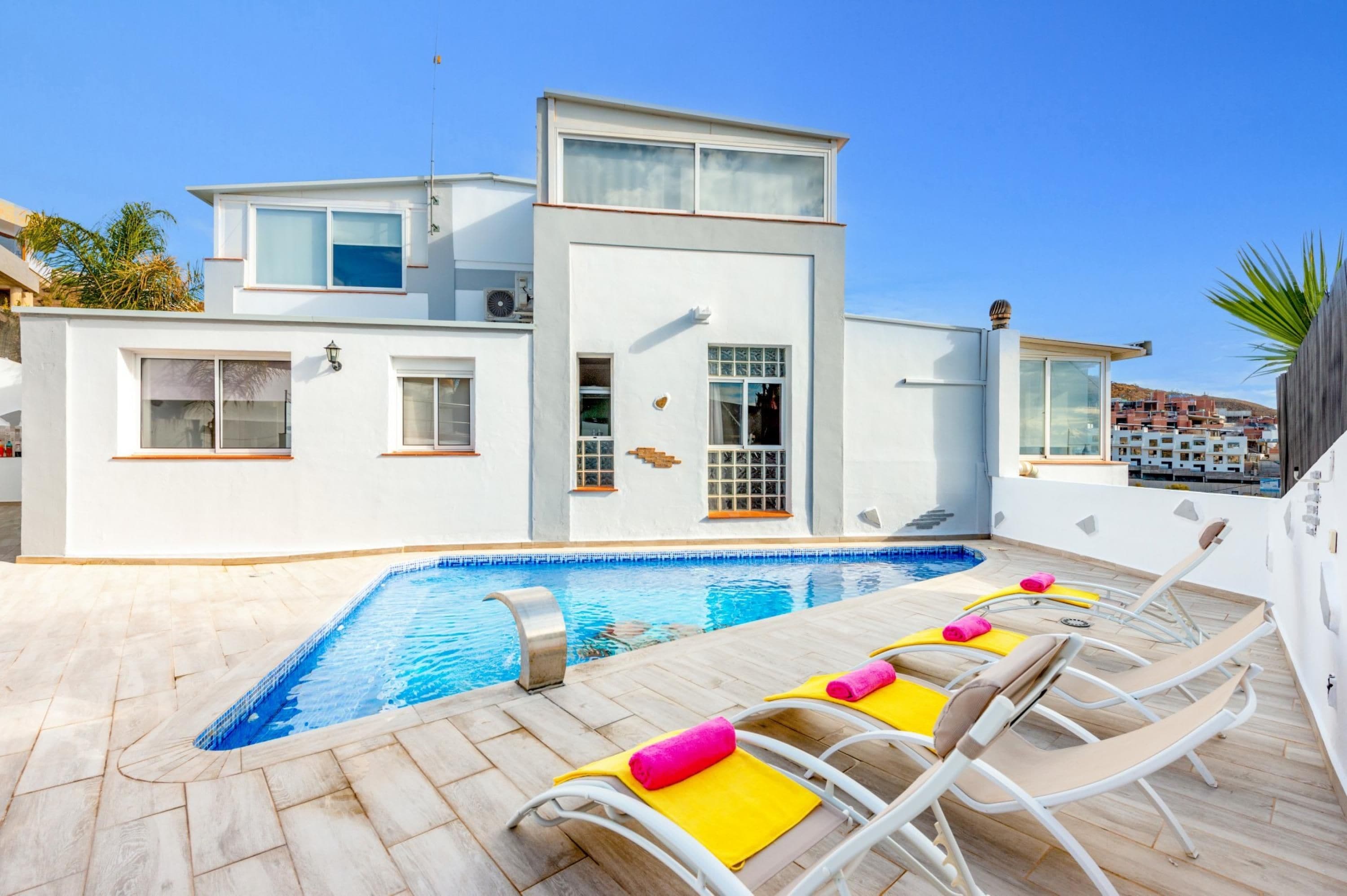 A modern two-story building with a swimming pool and sun loungers.