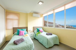 A hotel room with two beds, a window with a view of the sea and buildings, and an air conditioning unit on the wall. - Villa Marrakech in Torrox Costa (Torrox)