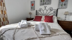 A neatly made bed with white linens and red pillows, a bedside table with a lamp, and artwork on the wall. - Villa Paco by At Home Costa del Sol (Torrox)