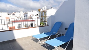 A balcony with two blue lounge chairs, a white wall, and a view of buildings in the background. - Atico Platero Nerja by At Home Costa del Sol (Nerja)