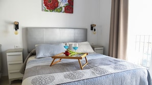 A neatly made bed with a patterned bedspread, a bedside table with a lamp, and a tray with glasses and flowers on it. - Atico Platero Nerja by At Home Costa del Sol (Nerja)