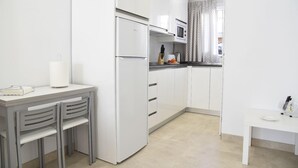 Une cuisine compacte avec des meubles blancs, un micro-ondes encastré et un petit coin repas comprenant une table et deux chaises.