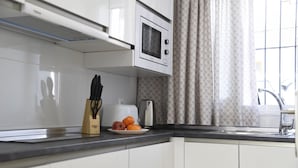 Une cuisine avec des meubles blancs, un four à micro-ondes, un grille-pain et un panier à fruits contenant des oranges et des pommes.