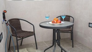 Une petite pièce avec deux fauteuils en osier, une table ronde sur laquelle se trouve une assiette de fruits et deux verres contenant un liquide bleu, et un tuyau raccordé à une prise murale.