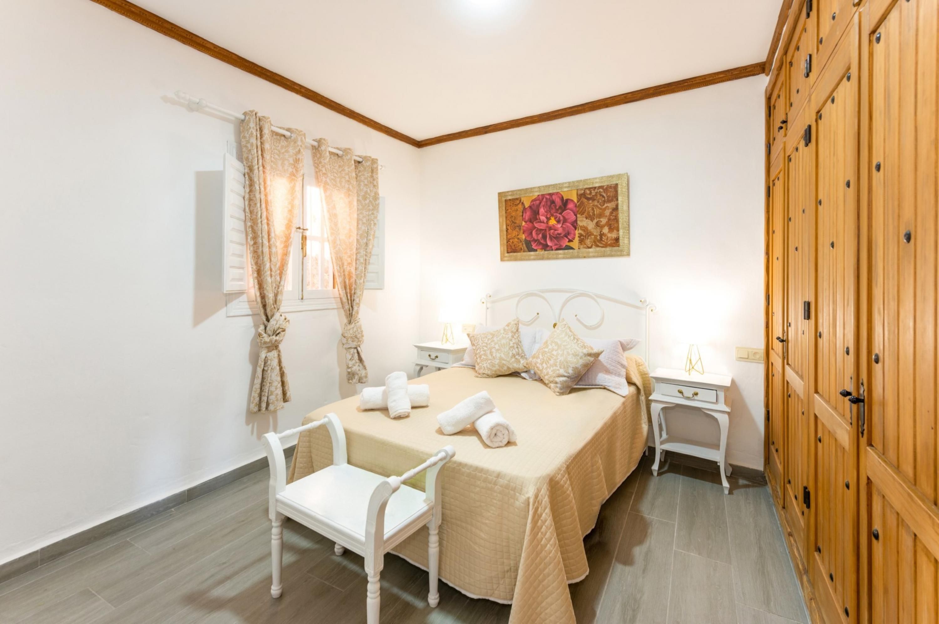 Une chambre à coucher comprenant un lit, deux tables de chevet, une chaise, une armoire et une fenêtre avec des rideaux.