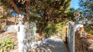 A gated entrance with stone walls and a metal gate, leading to a pathway surrounded by trees. - Villa Las Palomas by At Home Costa del Sol (Torrox)