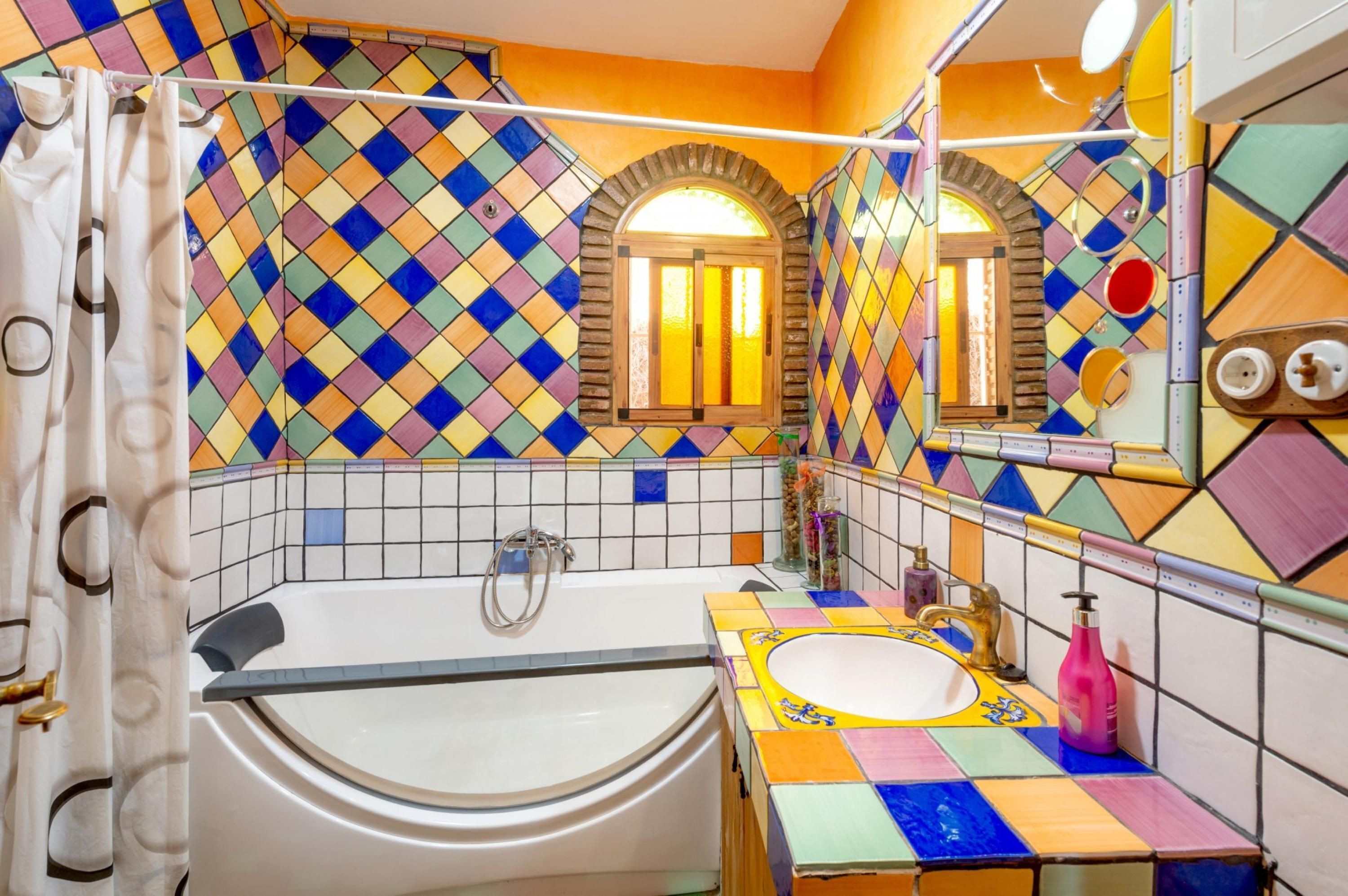 Un bagno con una parete in mosaico colorato, una vasca da bagno, un lavandino con uno specchio e una tenda da doccia.