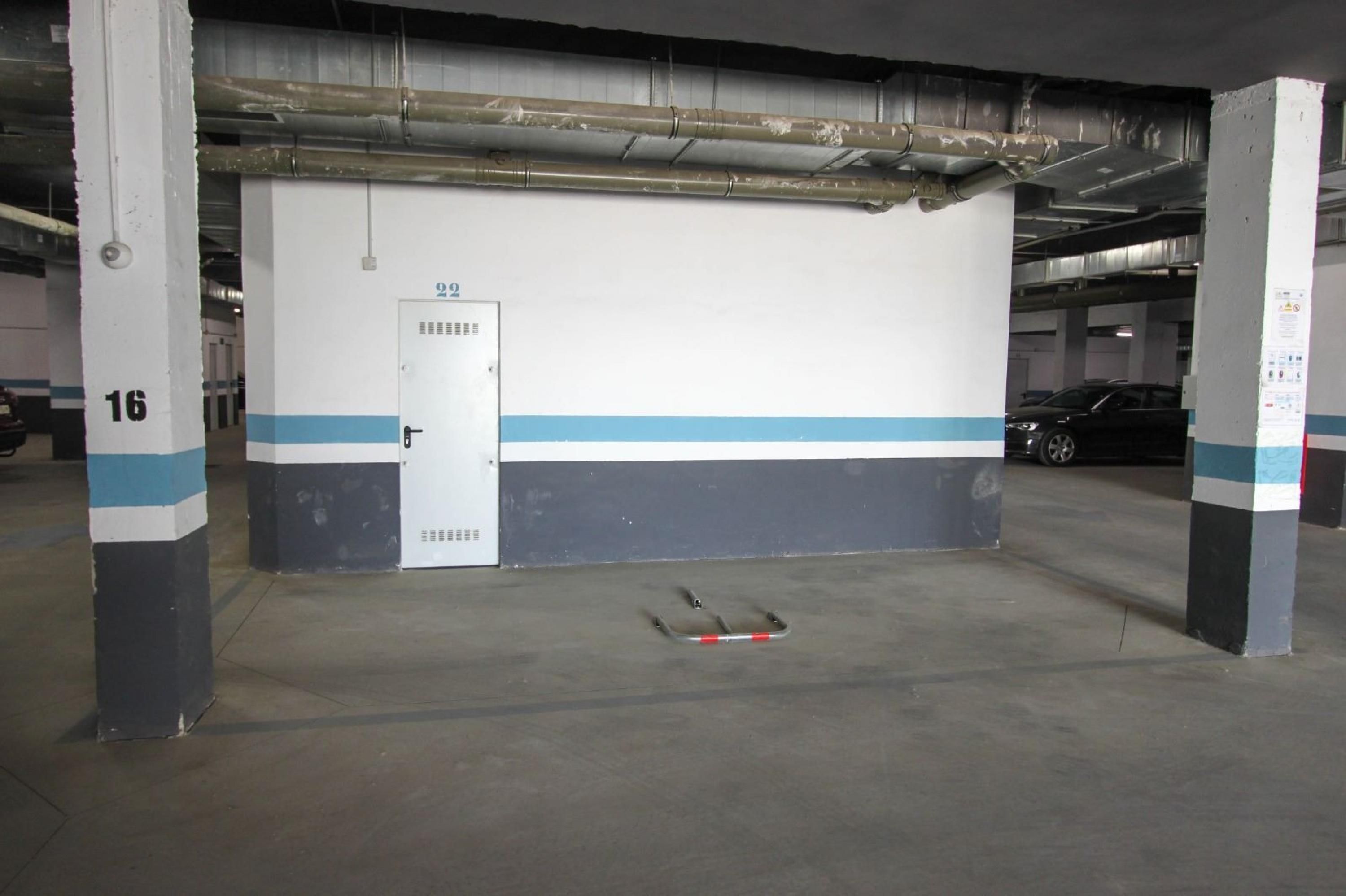 A parking garage with concrete pillars, a white door with a blue stripe, and a car parked in the background.