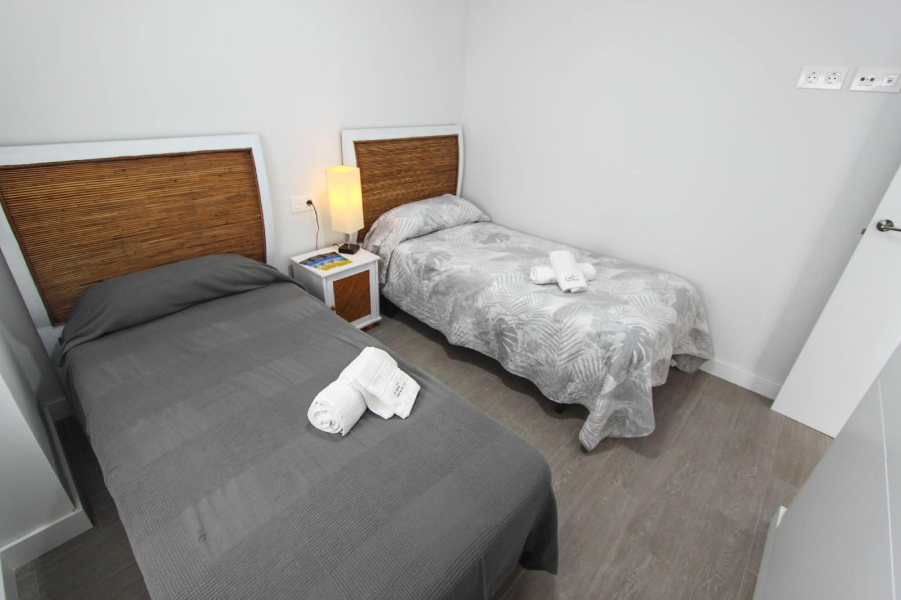 Ein Hotelzimmer mit zwei Betten, einem Nachttisch mit Lampe und einer weißen Wand mit Steckdosen.