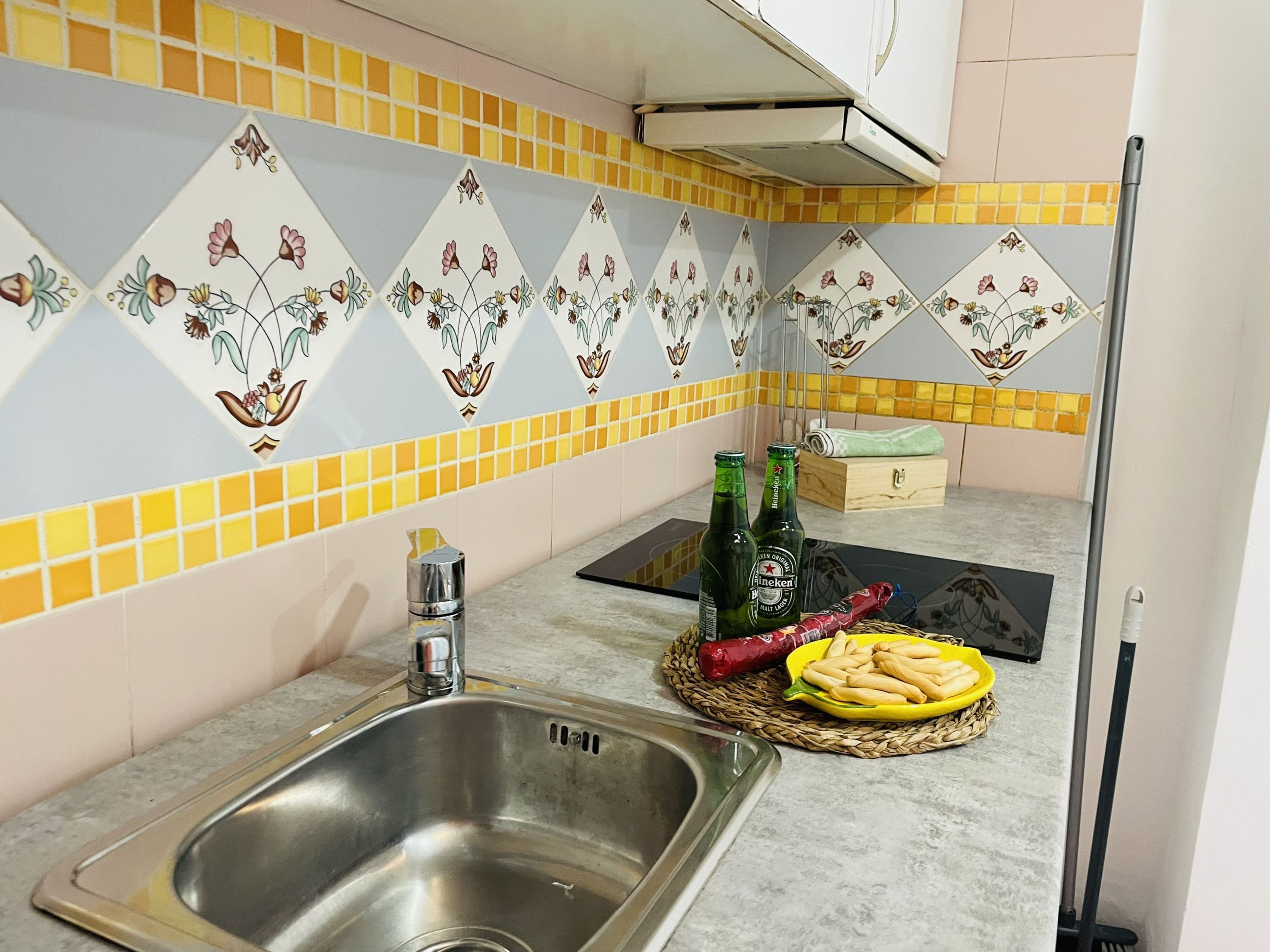 Una cocina con un lavamanos de acero inoxidable, dos botellas de cerveza Heineken, una cesta con pan y un chile rojo.