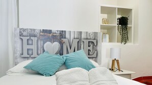 A neatly made bed with a 'HOME' sign, a teal pillow, and towels with 'at home costa del sol' text.