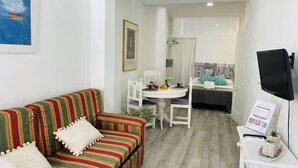 A cozy living room with a striped sofa, a dining table, and a TV mounted on the wall.