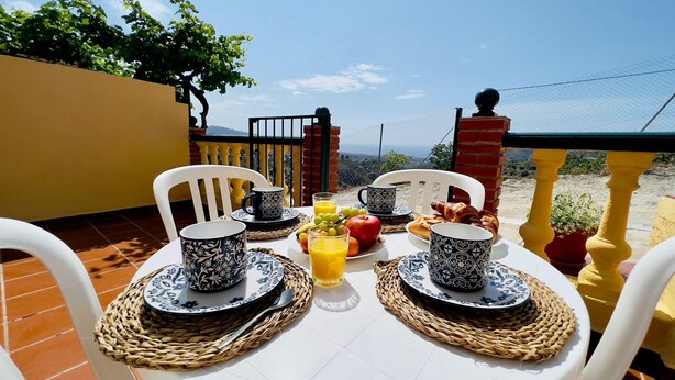 Een ontbijttafel met uitzicht op de bergen, witte stoelen en servies met een patroon.