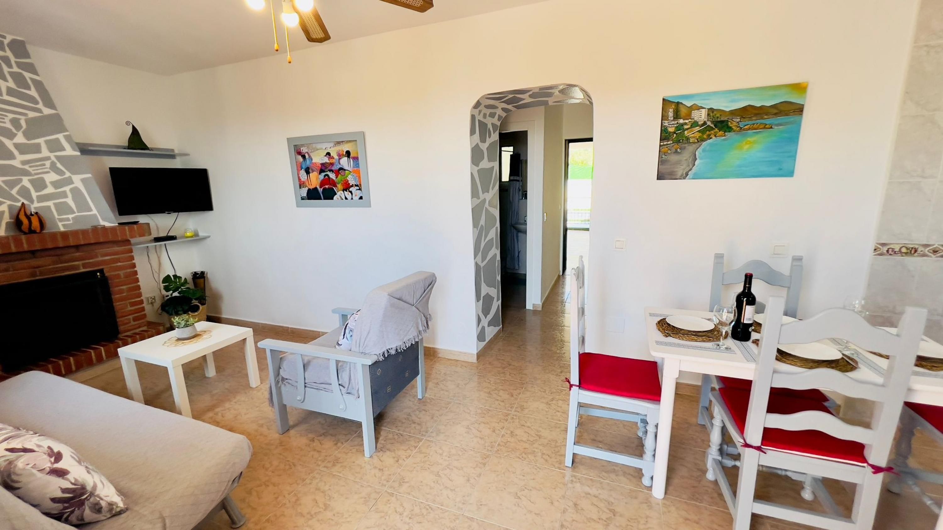Un salon avec une cheminée, un téléviseur, un canapé, une table à manger avec des chaises et des œuvres d’art accrochées aux murs.
