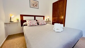 Een keurig opgemaakt bed met bloemenkussens, een nachtkastje met een lamp en een houten garderobe.
