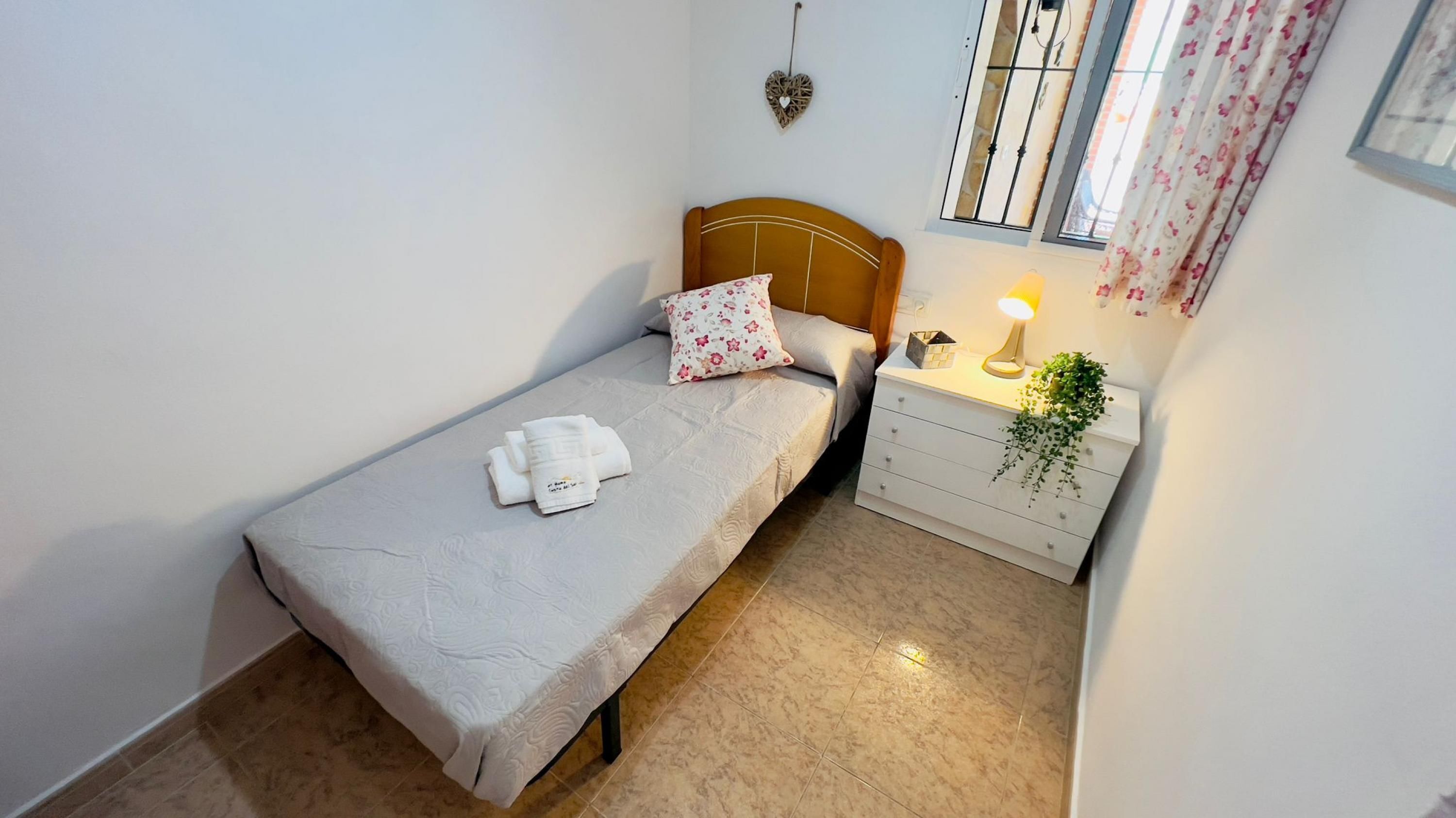 A small, neatly arranged bedroom with a single bed, a bedside table with a lamp, and a window with curtains.