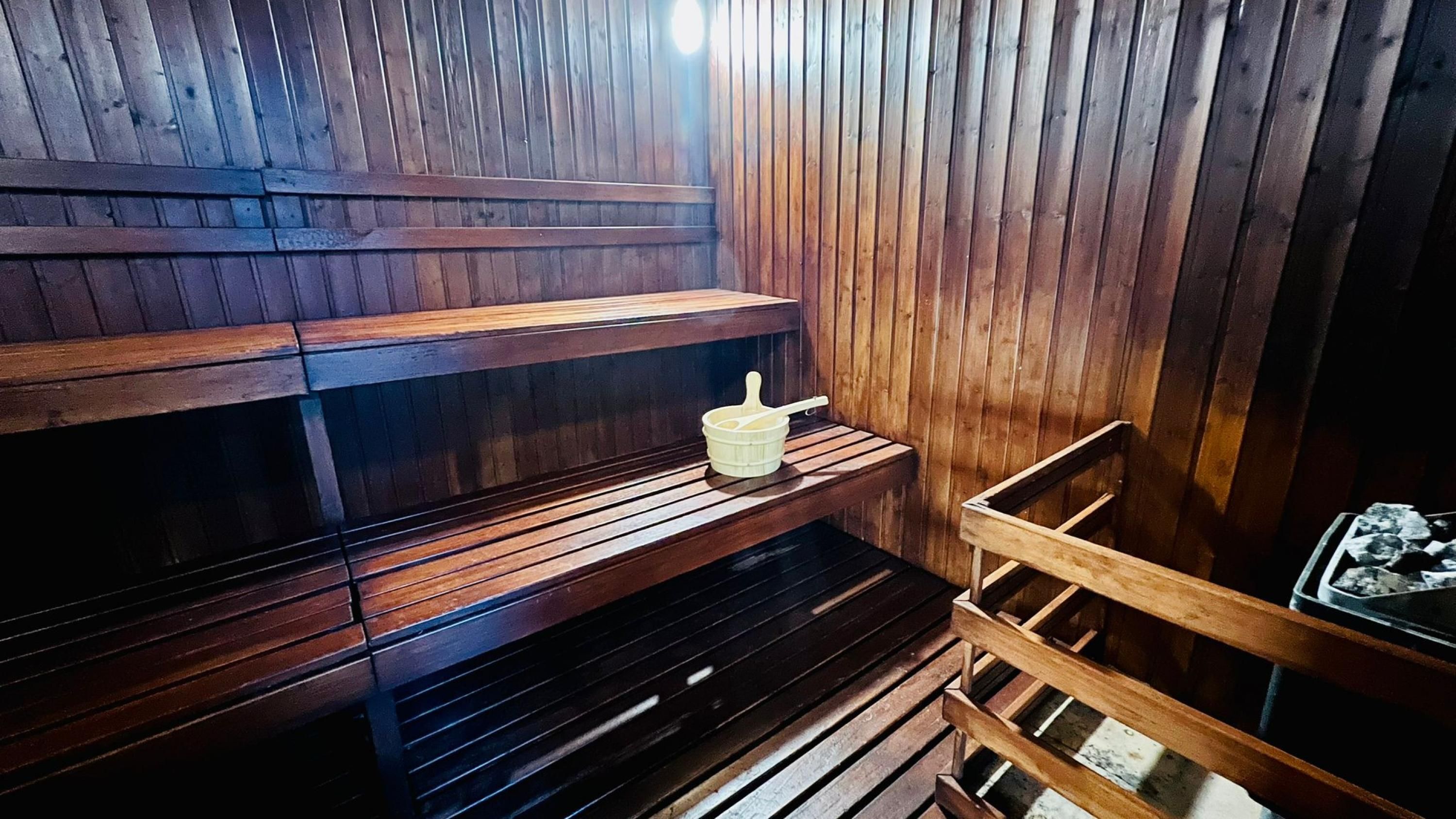 A sauna with wooden benches and a small shelf with a bucket and brush.