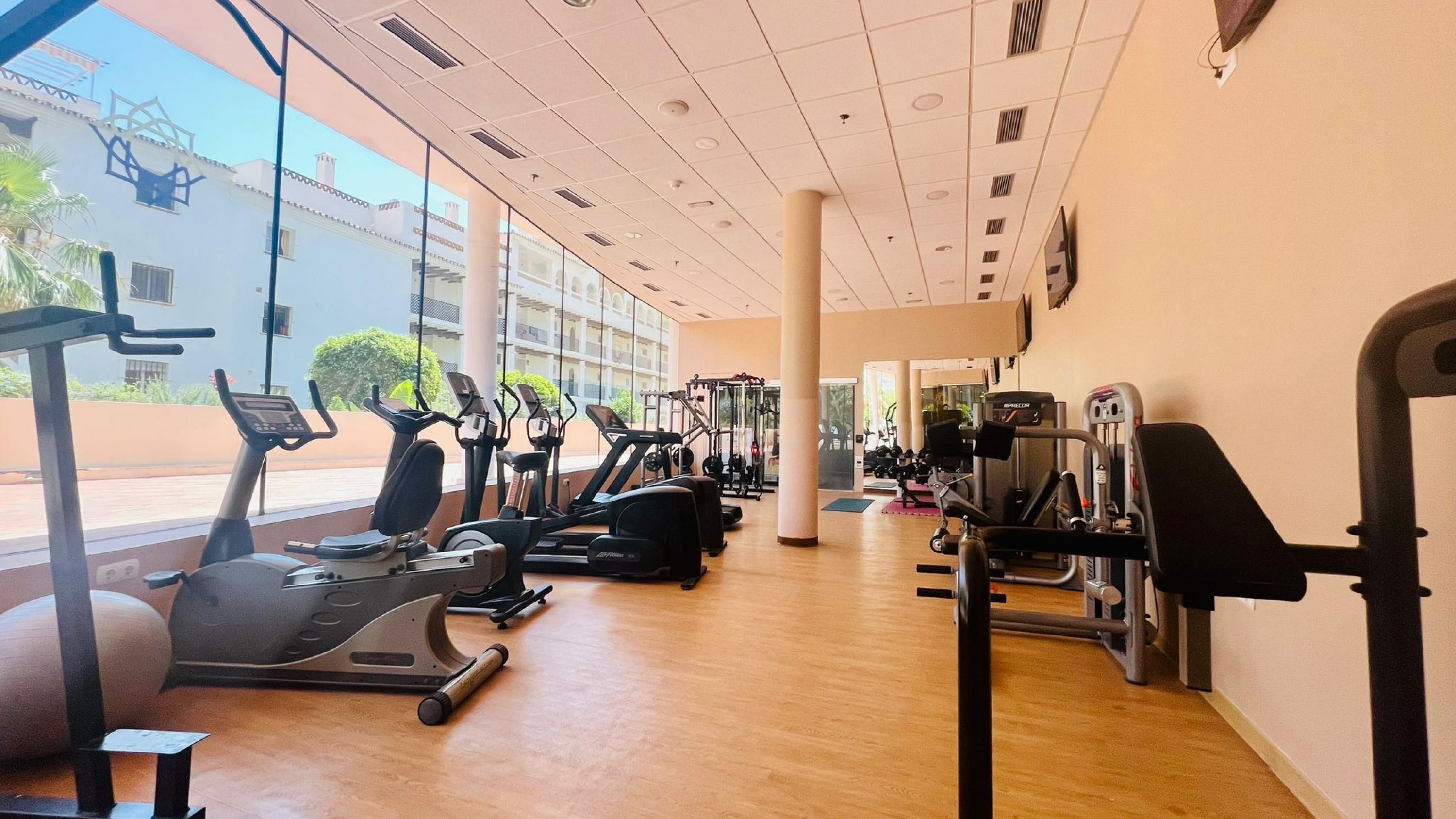 A gym with cardio machines, weight equipment, and large windows offering views of the outside.