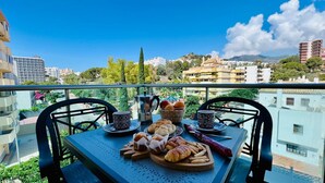Un balcon avec une table préparée pour le petit-déjeuner, comprenant du pain, des viennoiseries et des fruits.