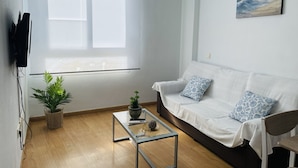 Una sala de estar moderna con un sofá blanco, dos almohadas estampadas, una mesita de centro, una planta en maceta y un cuadro en la pared.