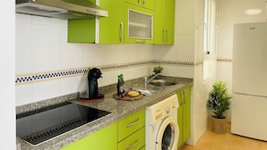 Una cocina moderna con gabinetes verdes, horno empotrado, lavadora y refrigerador.
