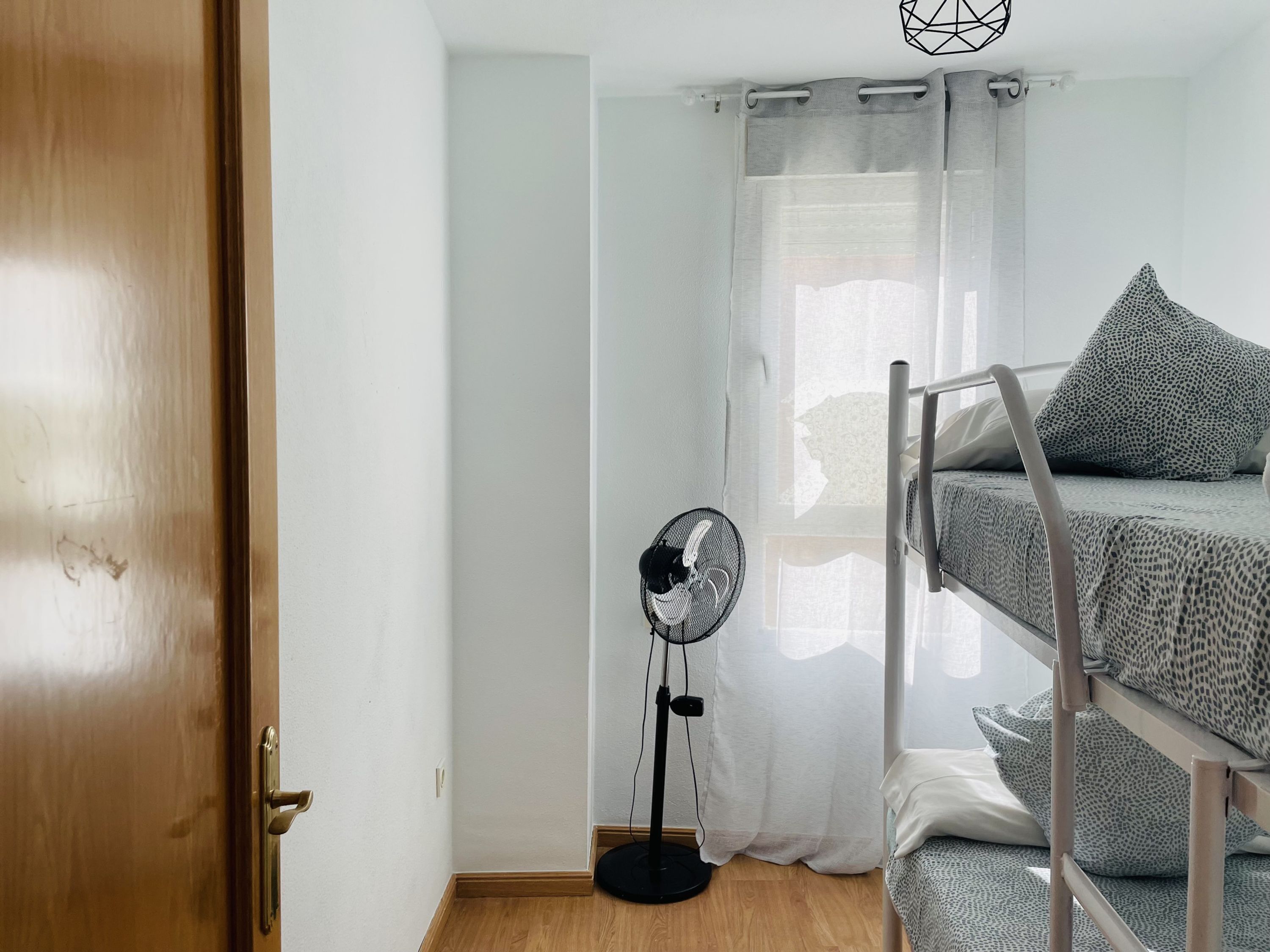 A room with a bunk bed, a standing fan, and a door.