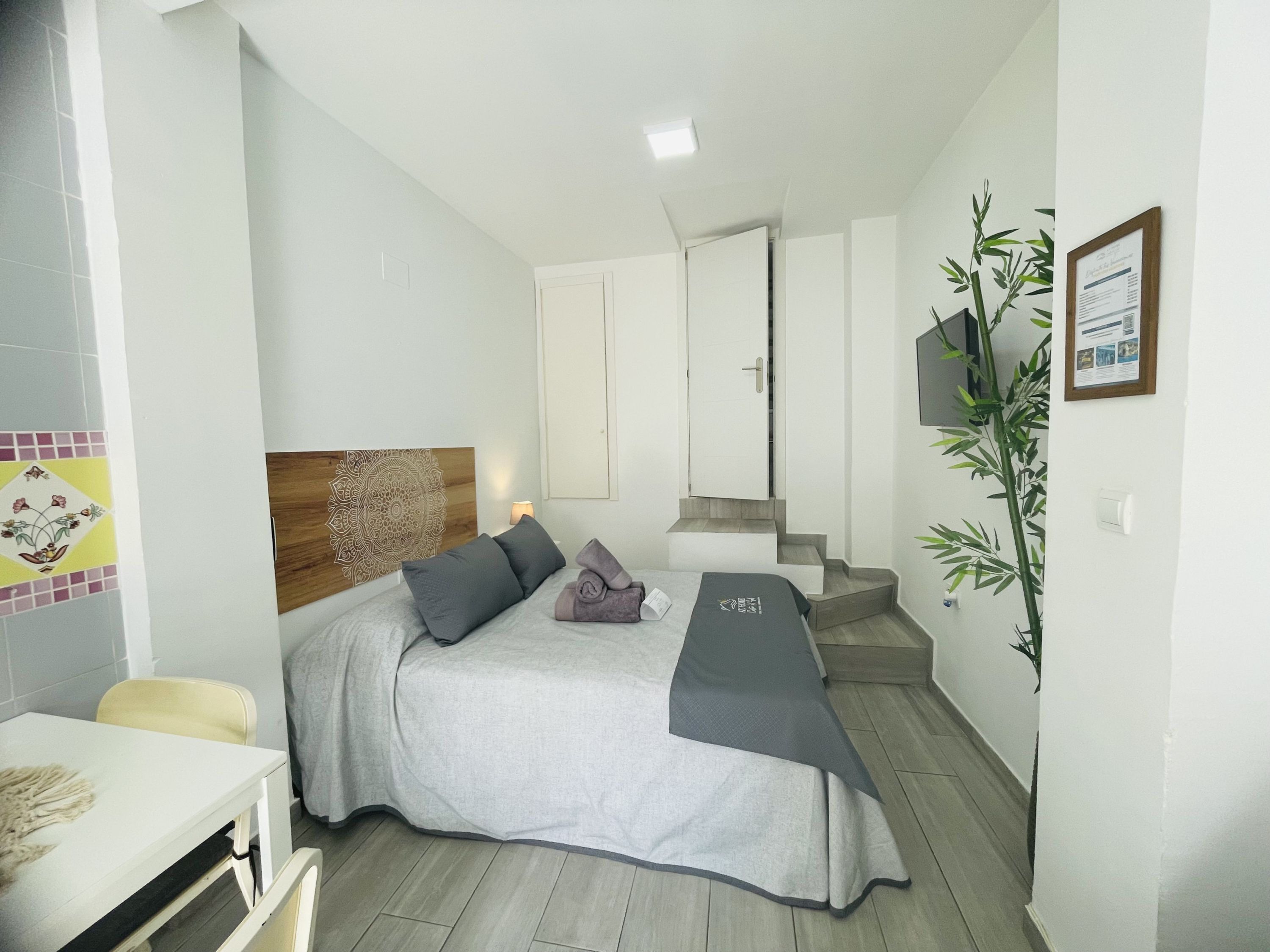 A hotel room with a bed, a desk, a chair, a plant, and a staircase.