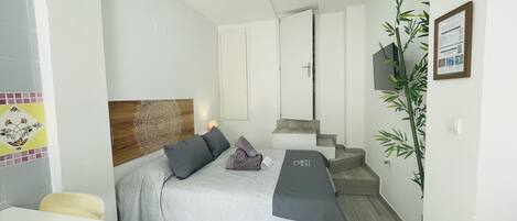 A hotel room with a bed, a desk, a chair, a plant, and a staircase.