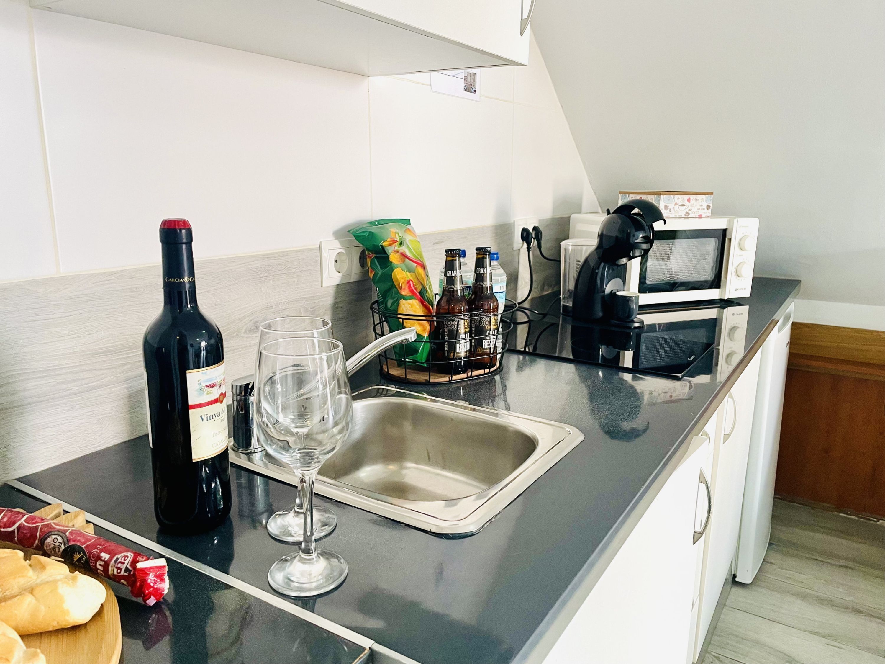 Een keuken met een wijnfles, twee glazen, een magnetron en een koffiezetapparaat.