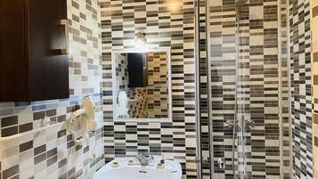 A bathroom with a tiled wall, a sink, a mirror, a shower, and a telephone.
