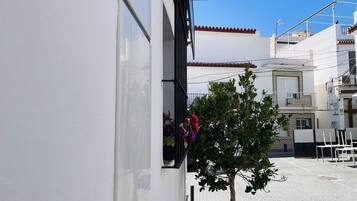 Et potteprydet træ med blomster, en hvid bygning med balkon og en klar blå himmel.