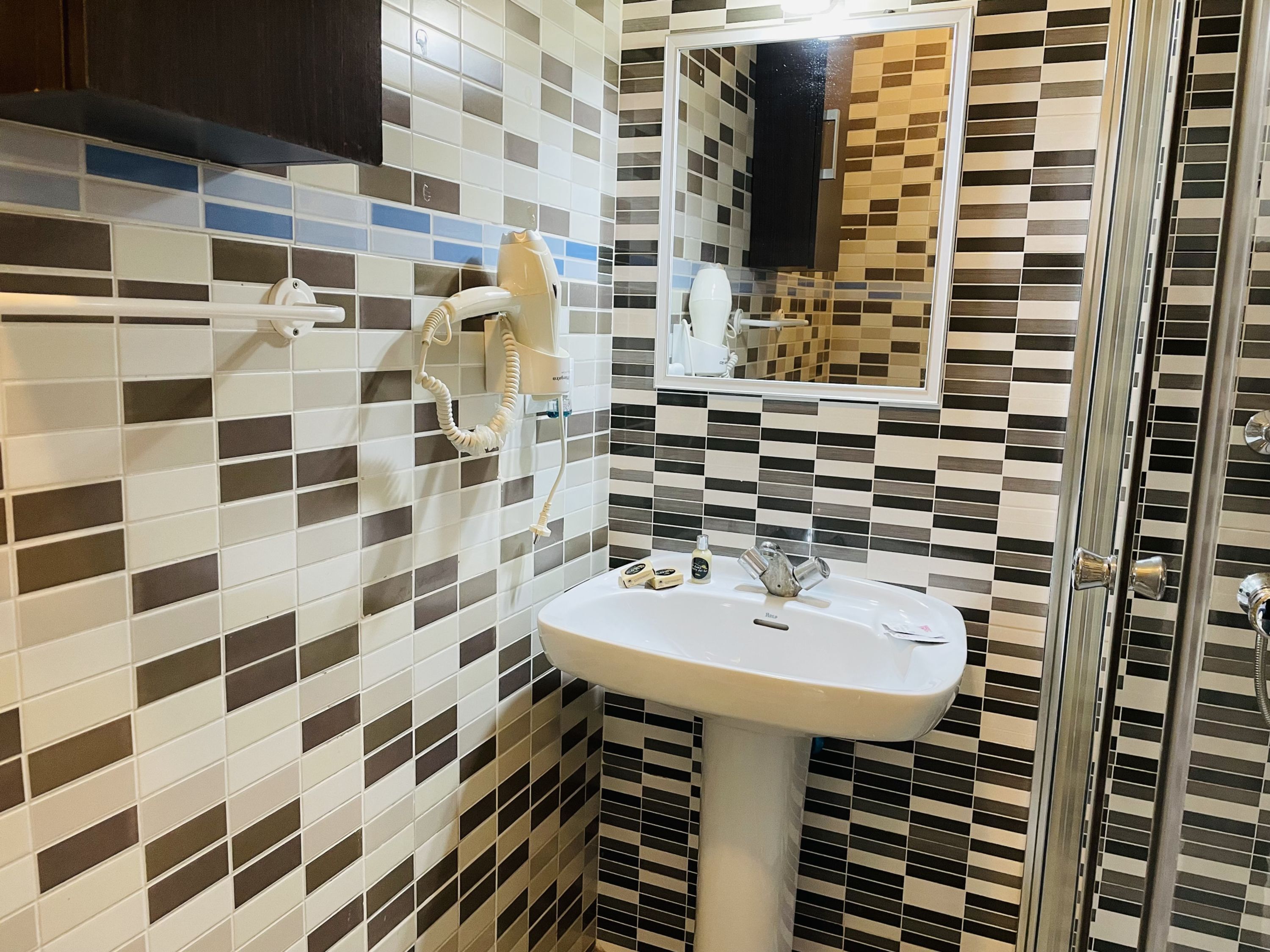 Un baño con pared de azulejos, lavamanos, espejo y secador de pelo.