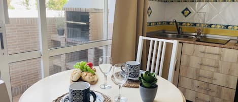 A dining area with a round table set for two, featuring a potted plant, a bottle of wine, and a bowl of grapes.