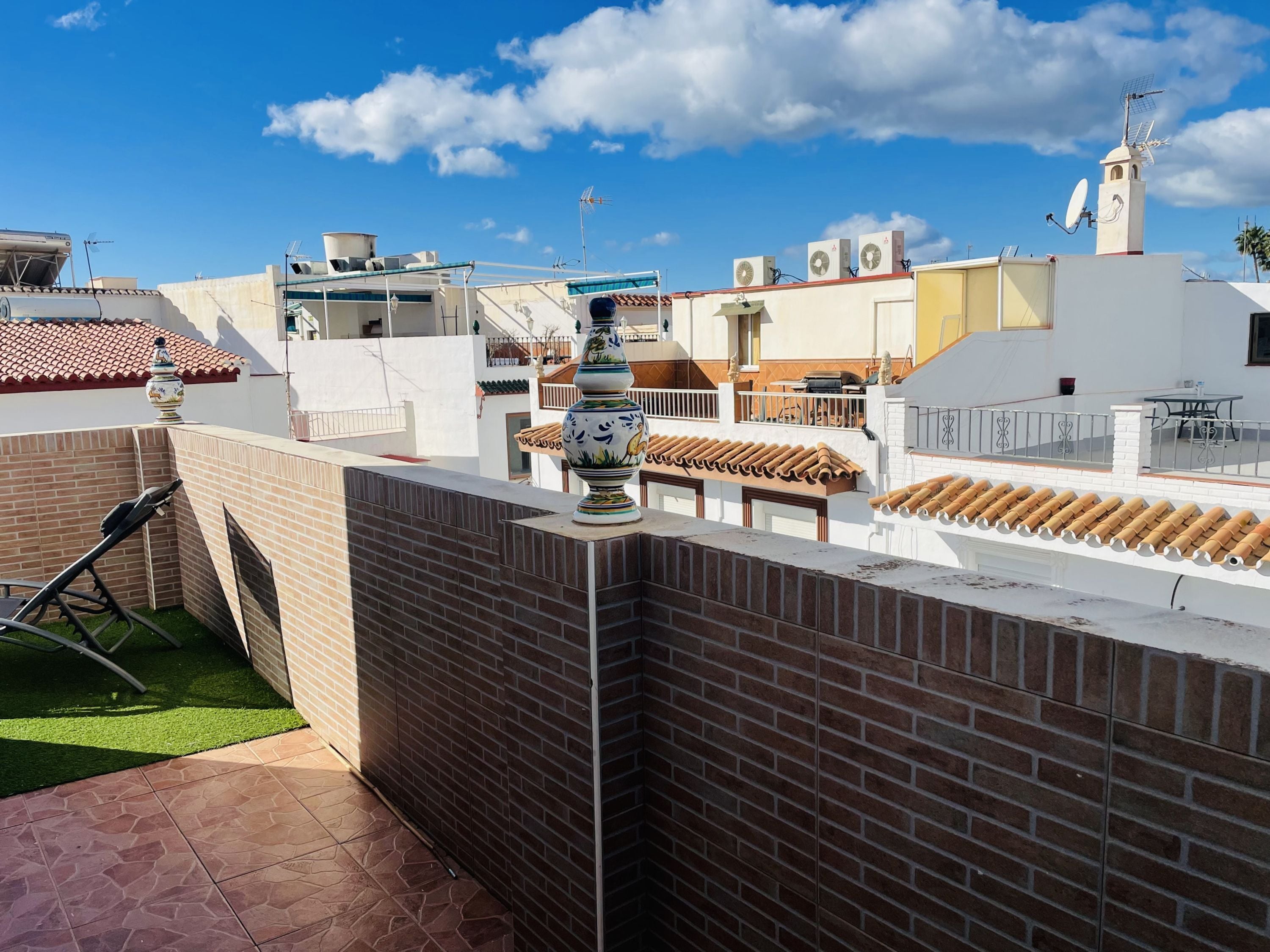 A rooftop terrace with a brick wall, a decorative vase, and a table.