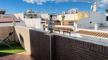 A rooftop terrace with a brick wall, a decorative vase, and a table.