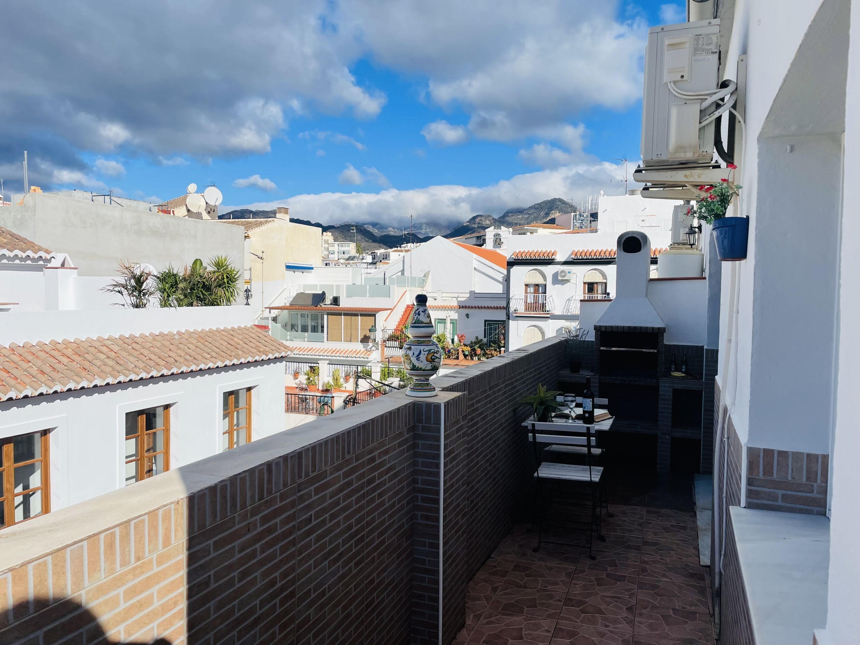 Una terraza en la azotea con un muro de ladrillo, una mesa pequeña con sillas y una planta en maceta.