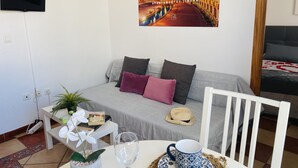 A cozy room with a sofa, a dining table with a cup and glass, and a poster of Sevilla. - Apartamento Sevilla Jimena by At Home Costa del So (Nerja)