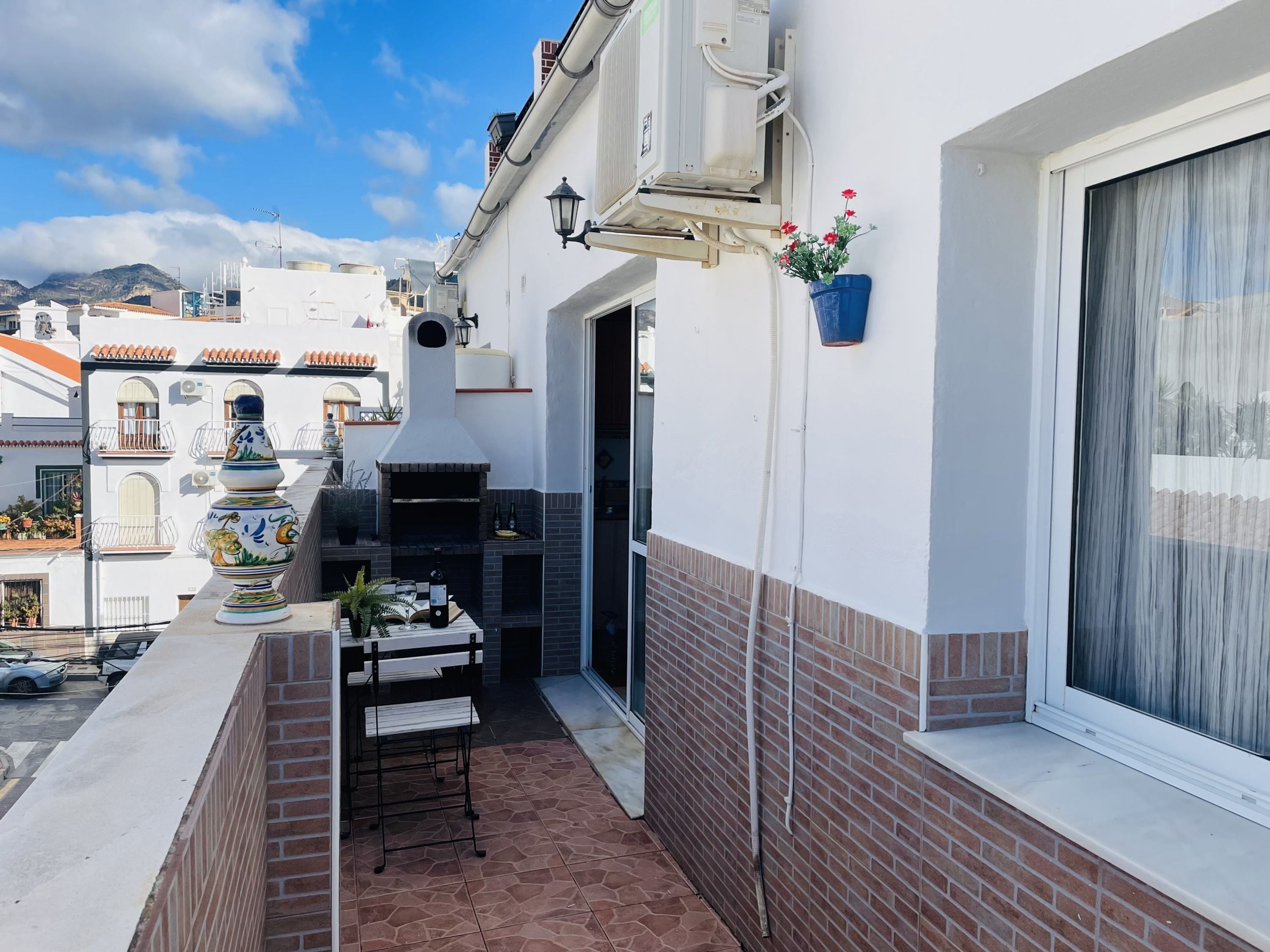 A balcony with a brick floor, a small table with chairs, a decorative vase, and a potted plant.