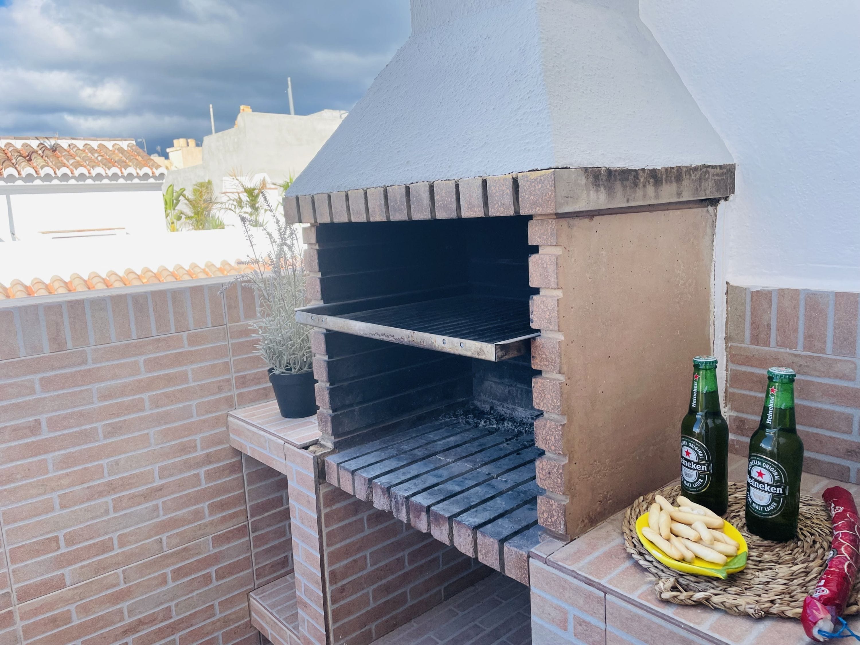 An outdoor brick oven barbecue setup with two Heineken beer bottles and a plate of fries.