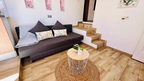 Una sala de estar moderna con un sofá gris oscuro, dos cojines, una mesita de centro de madera con una planta y una alfombra tejida.