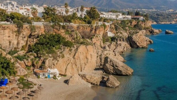 Una playa costera con acantilados rocosos, aguas azul turquesa y un pequeño bote en la arena.