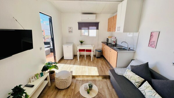 A compact living space with a kitchenette, a dining area, and a seating area with a sofa and a TV.