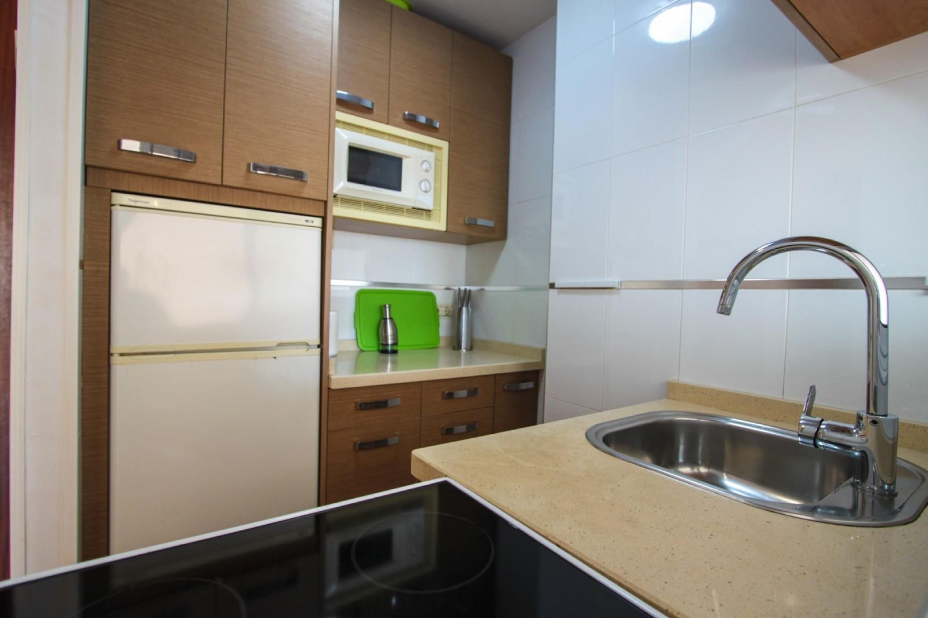 Une cuisine avec des meubles de rangement en bois, un four à micro-ondes, un grille-pain vert et un évier en acier inoxydable.