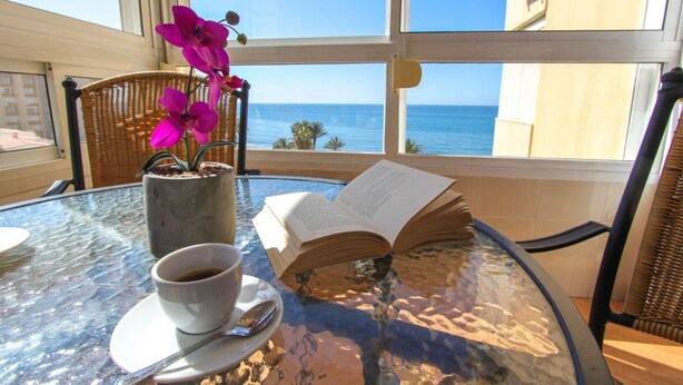 A glass table with a book, a cup of coffee, and a flower vase.