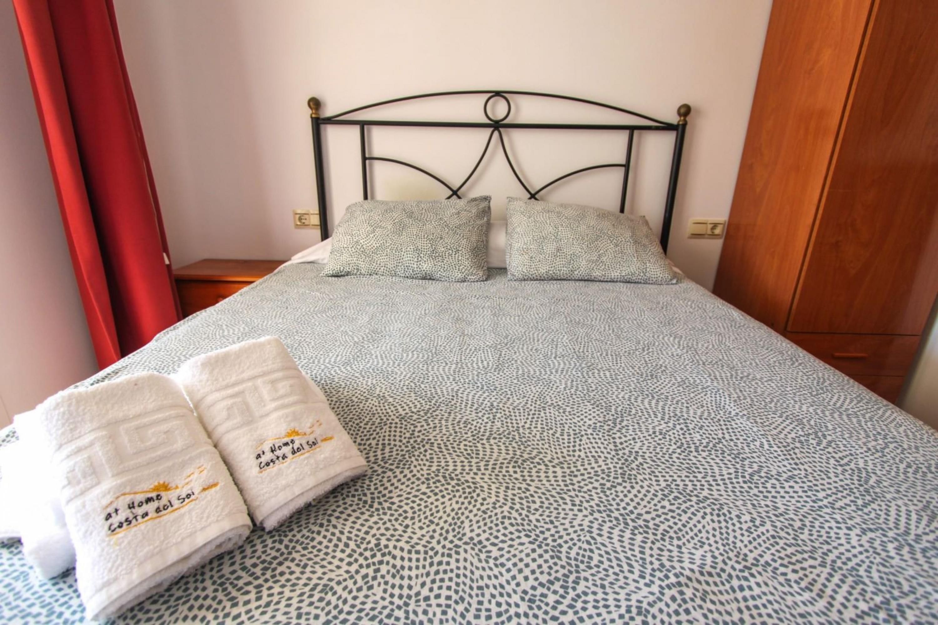 A neatly made bed with a patterned bedspread, two pillows, and two folded towels with text on them.