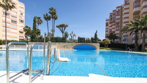 A swimming pool with a stone archway, surrounded by palm trees and tall buildings.