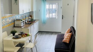 A compact kitchen with white cabinets, a microwave, and a small dining area with a table and chairs. There is a sofa with orange pillows in the adjacent living area.