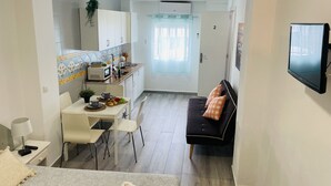 A compact living space with a kitchenette, a dining area, a sofa, and a TV mounted on the wall.