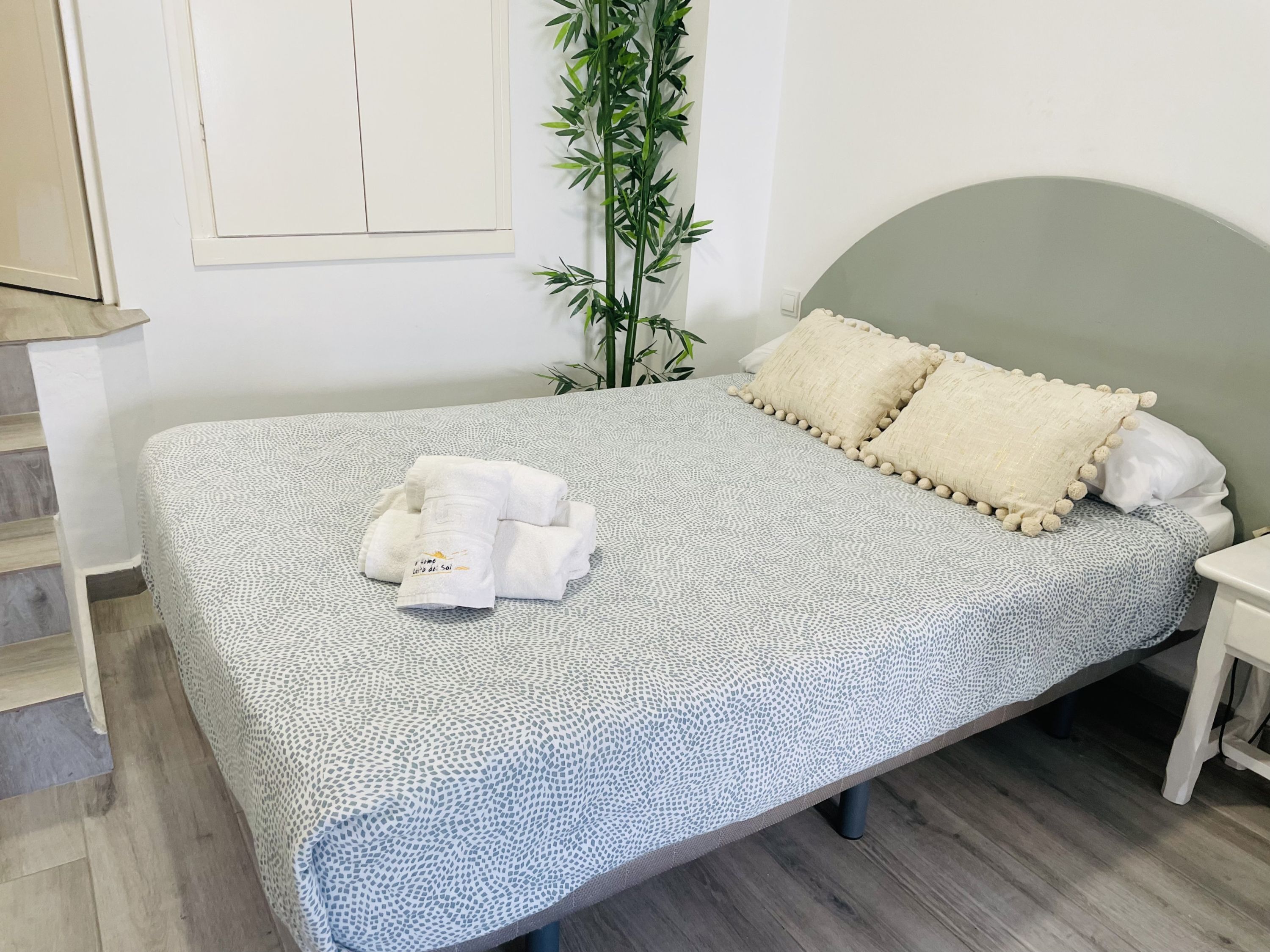 Un lit bien fait, avec une couvre-lit à motifs, deux oreillers décorés de pompons et une serviette pliée posée sur le lit.
