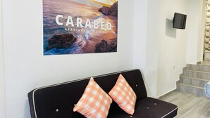 A modern waiting area with a black sofa, two orange checkered cushions, and a large scenic poster of a sunset over the sea.